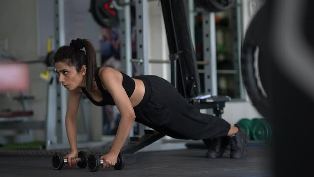 A young indian woman fit doing push ups at gym. active, fit, sporty and healthy lifestyle, exercising at gym concept.
