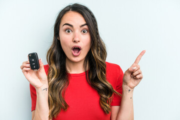 Fototapeta premium Young caucasian woman holding car keys isolated on blue background pointing to the side