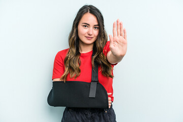 Young caucasian woman with broke hand isolated on blue background standing with outstretched hand showing stop sign, preventing you.