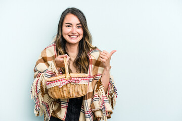 Young caucasian woman holding a picnic basket isolated on blue background smiling and raising thumb...