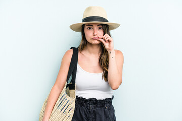 Young caucasian woman holding beach bag isolated on blue background with fingers on lips keeping a secret.