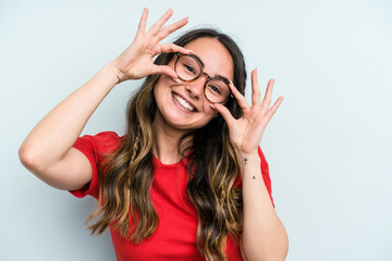Young caucasian woman isolated on blue background showing okay sign over eyes