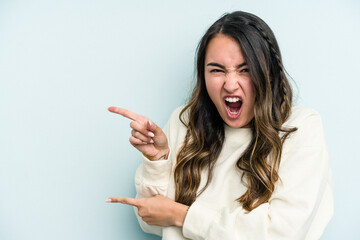 Young caucasian woman isolated on blue background pointing with forefingers to a copy space,...