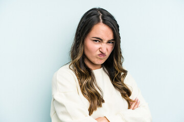 Young caucasian woman isolated on blue background frowning face in displeasure, keeps arms folded.