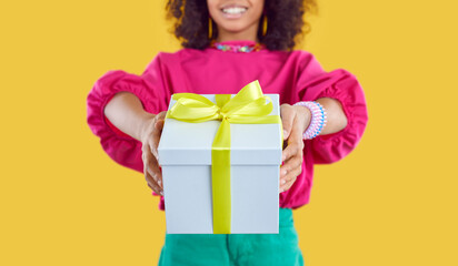 Happy little kid giving you a cool present. Cropped shot of an Afro American child holding a white gift box tied with a beautiful yellow bow. Birthday party, surprise, holiday sale concept