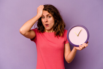 Young caucasian woman holding a clock isolated on yellow background being shocked, she has...