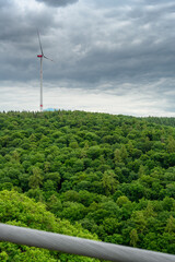single windmill over green forest and in front of cloudy sky