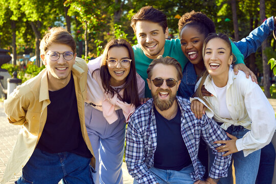 Cheerful friends posing for a group photo in a summer park. Diverse group of happy beautiful young people in casual clothes meet up in the park, have a good time and have fun all together