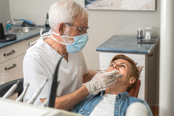 Mature experienced male doctor in glasses and face mask performs a regular examination of the patient. Doctoral practice. Patient healthcare