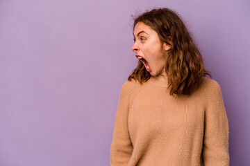 Young caucasian woman isolated on purple background shouting very angry, rage concept, frustrated.