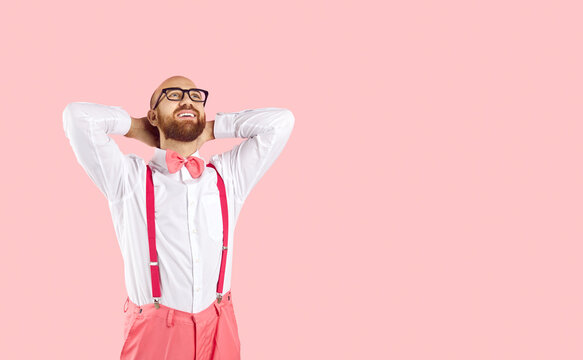 Happy bald man dreaming and smiling. Handsome guy with ginger beard, in white shirt, bow tie, pants with suspenders and glasses imagining something pleasant isolated on blank solid pink background