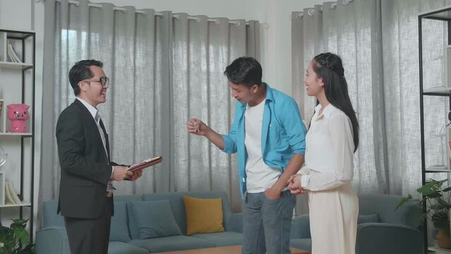 Asian Man Receiving The Keys From A Real Estate Agent Before Showing To A Woman Who Stands With Him In The House For Sale
