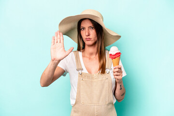 Young caucasian pregnant woman holding an ice cream isolated on blue background standing with outstretched hand showing stop sign, preventing you.