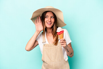 Young caucasian pregnant woman holding an ice cream isolated on blue background trying to listening a gossip.