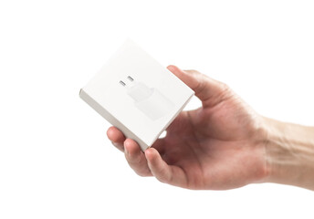 The hand holds a white box with a charger for a smartphone. Close up. Isolated on a white background