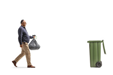 Full length profile shot of a mature man carrying a plastic waste bag and walking towards a dustbin