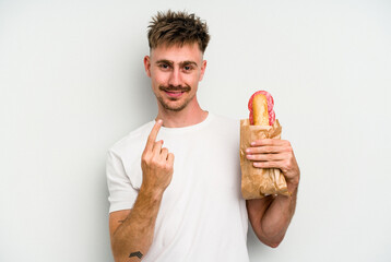 Young caucasian man holding a sandwich isolated on white background pointing with finger at you as if inviting come closer.