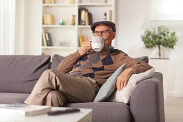 Obraz premium Elderly man relaxing on a sofa at home and drinking tea