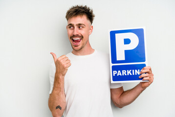 Young caucasian man holding parking placard isolated on white background points with thumb finger...