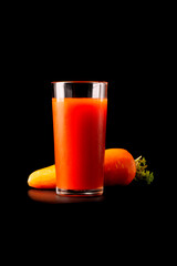 Carrot juice in a tall glass glass with natural fresh tomatoes on a black background.