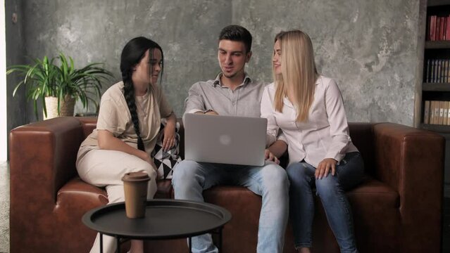 Young guy and two girls sit on the couch and look at a laptop. Online Shopping