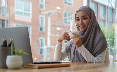 Beautiful muslim businesswoman boss manager wearing hijab drinking hot coffee and working at modern office.