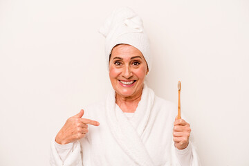 Middle age caucasian woman wearing a bathrobe holding toothbrush isolated on white background person pointing by hand to a shirt copy space, proud and confident