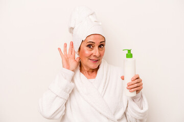 Middle age caucasian woman wearing a bathrobe holding body cream isolated on white background trying to listening a gossip.