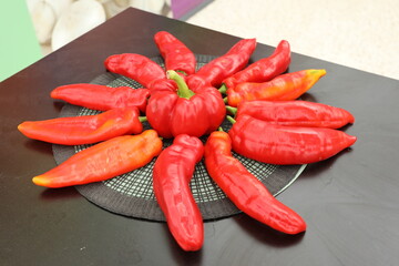 A white plate of veggies with Bell peppers, yellow pepper, and aubergine on a black table