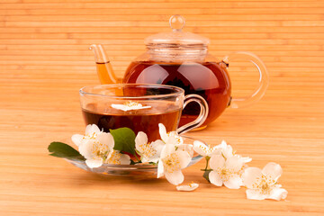 Jasmine tea in glass cup and fresh flowers, close-up on bamboo mat background.