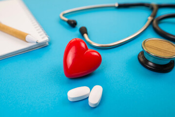  Red heart with a stethoscope and pills on a blue background.