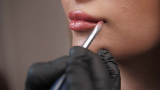 Makeup artist applies lipstick and gloss to a young girl's lips in a beauty salon.Close up.