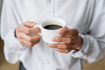 cropped view of woman holding cup of black and hot coffee in hands.