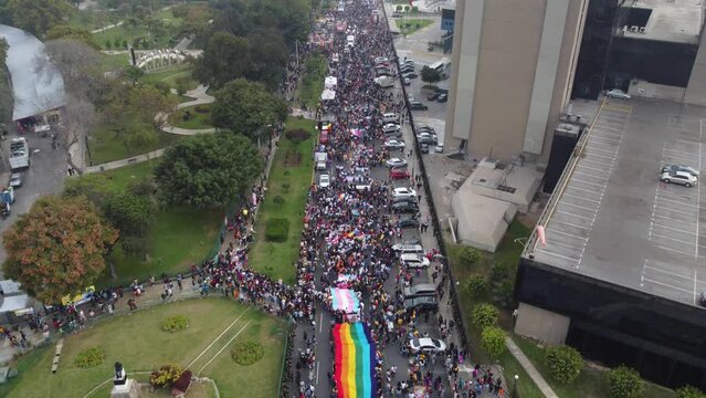 Drone video of people in the street gathering to celebrate pride month in Lima, Peru. A rainbow flag and a trans flag can be seen. Drone flying backwards.