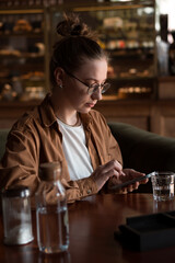 Young smiling woman sitting in cafe drinking coffe and using smartphone