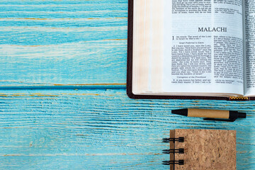 Malachi open Holy Bible Book on a rustic wooden table background with a notebook and pen. Copy...