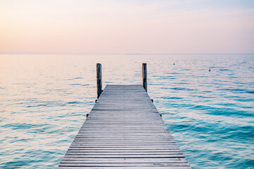 Wooden jetty pier on the sea at sunrise. Beautiful summer landscape in Italy