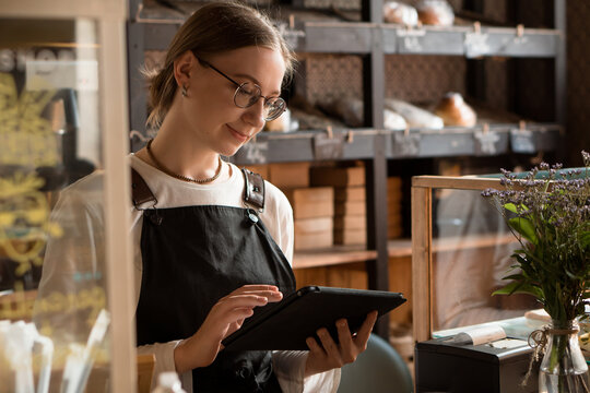 Young Woman Salesperson Working In Cafe Or Coffee Shop With Mobile Device And Cash Register