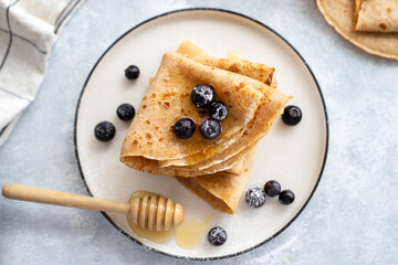 Freshly baked thin pancakes, crepes with blueberries and honey on blue plate. Healthy breakfast. Gray background