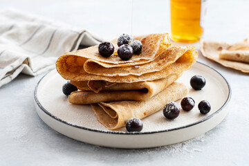 Freshly baked thin pancakes, crepes with blueberries and honey on blue plate. Healthy breakfast. Gray background