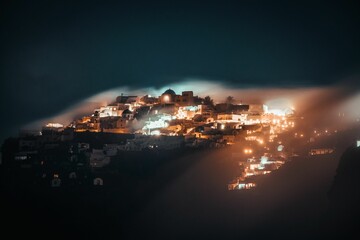 Breathtaking view of a mystical foggy cloud forming over Imerovigli in Santorini, Greece at night