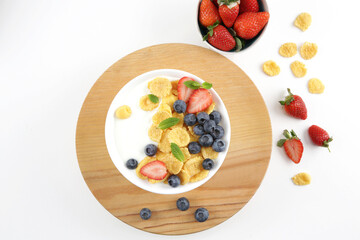 Corn flakes bowl next to strawberries on a white background