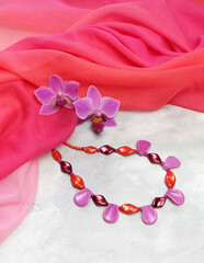 Czech glass beads with orchid flowers on a background of pink chiffon drapery, composition with handmade women's jewelry, with space for an inscription, selective focus, vertical orientation.