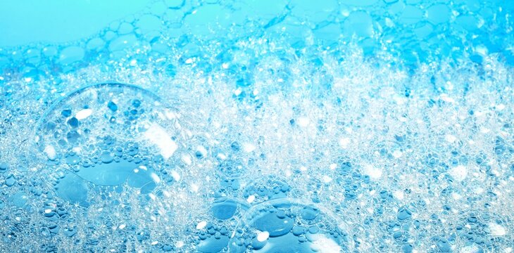 Closeup of transparent bubbles of soap foam covering surface of bright blue water