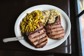 Smoked and grilled porkshops with a side of cheese spaetzle and mashed potatoes on a dinner plate with a large knife