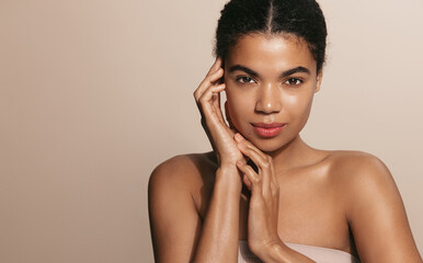Skin care routine. Dark skinned woman with perfect glowing body, head and shoulders, touches her...