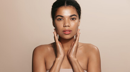 Close up shot of dark skinned woman with curly hair, appiles face cream on cheek, poses nude...