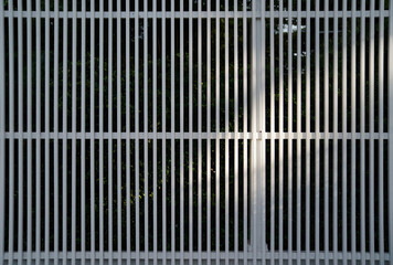 White metal fence that surrounded the garden illuminated in the sunlight shed by the trees shadows in the morning time.