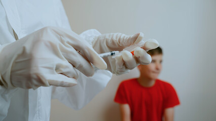Medical worker in protective suit collects medicine from plastic ampoule. Against background of blurred teen patient. Injection. Immunization. Vaccination against influenza, coronavirus and monkeypox