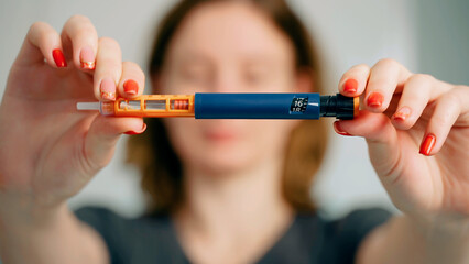 A diabetic woman dials the right dose of insulin on an insulin pen. Cartridge with liquid in syringe pen close up on blurred man background. Diabetes and prevention of diabetes complications. - obrazy, fototapety, plakaty